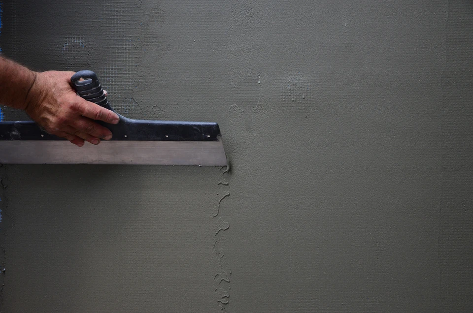 Un artisan applique un enduit de finition sur un mur extérieur à l'aide d'une taloche