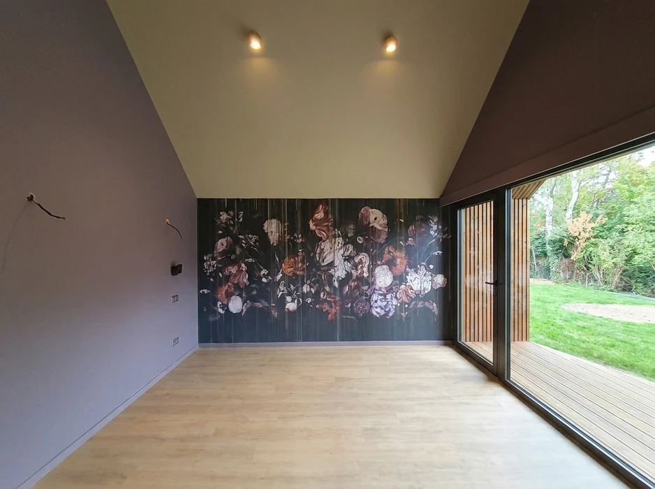 Pièce vide aux murs gris-lavande, sol en parquet stratifié chêne clair, plafond cathédrale blanc