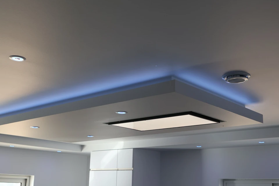 Artisan en tenue professionnelle et équipement de sécurité sur un chantier intérieur en cours de rénovation, montrant un espace de travail avec plusieurs types de travaux visibles : isolation thermique partiellement visible sur les murs, mise en place de cloisons sèches, et éléments de revêtement prêts à être installés. L'artisan est positionné dans cet environnement multi-tâches, illustrant la diversité des compétences requises pour un projet de rénovation intérieure complet.